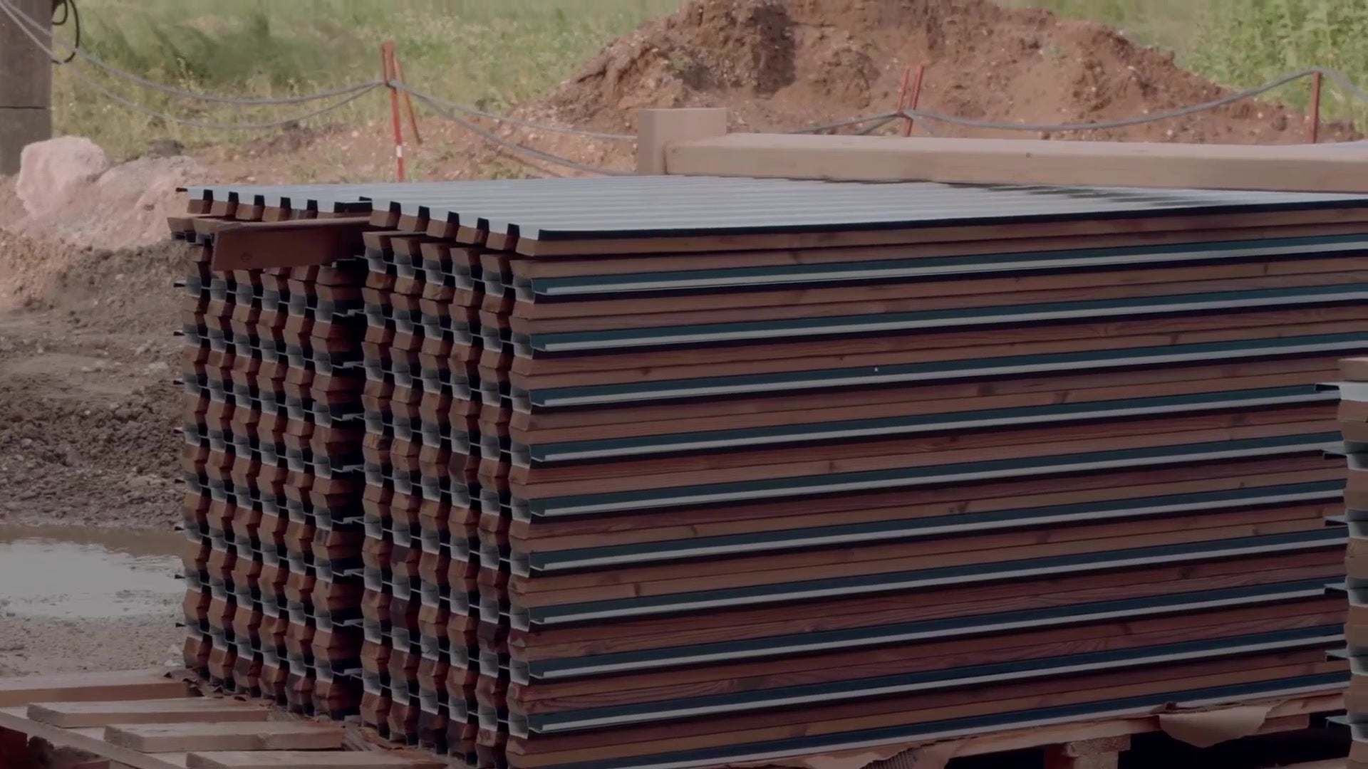 Stacks of pre-assembled Aluwood slat panels on pallets at a building site